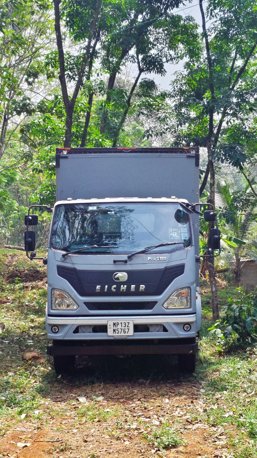 Front view of the cab with the habitat body behind, parked under forest cover.