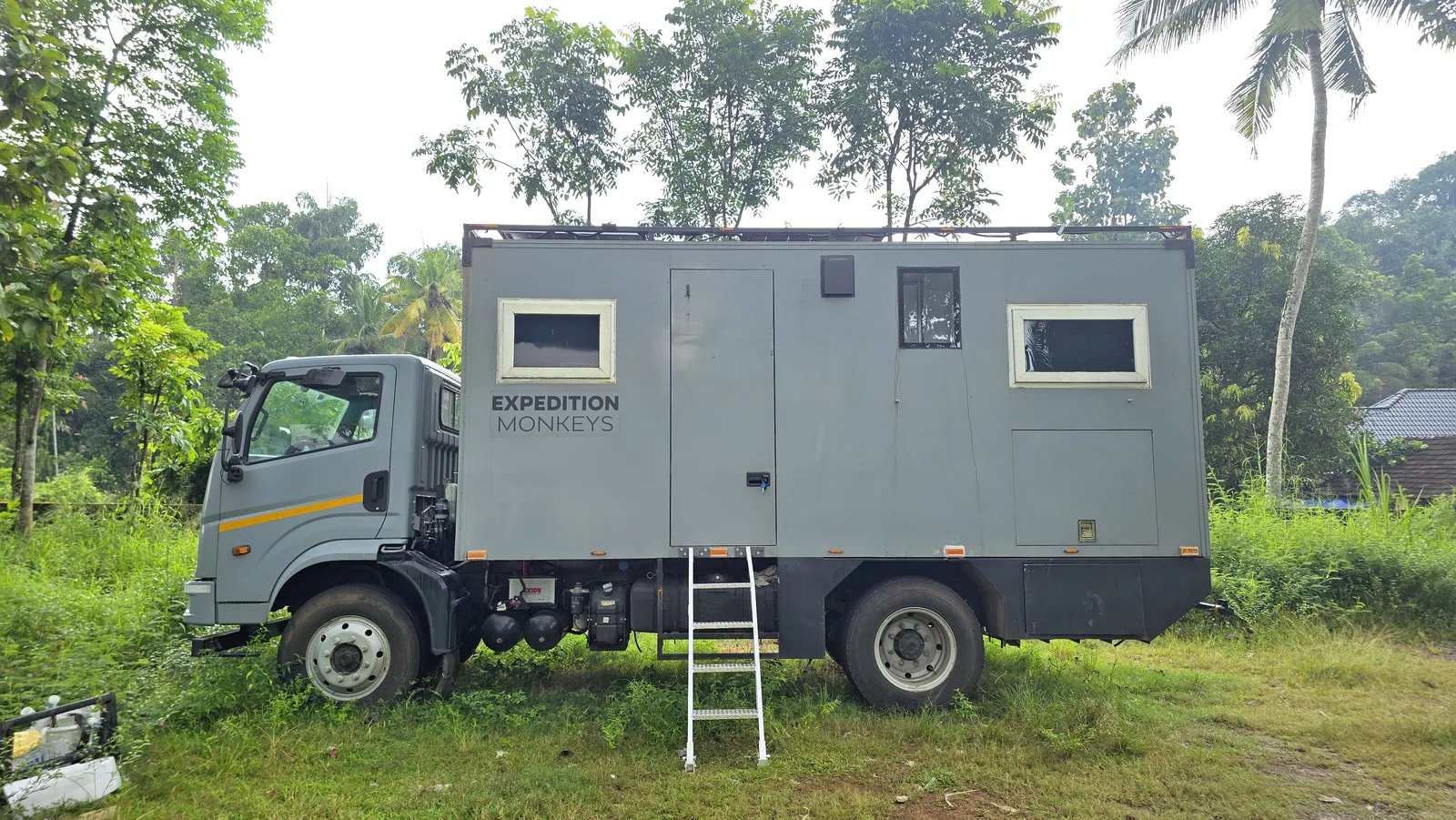 Rear three-quarter view of the camper body with ladder deployed on grass.