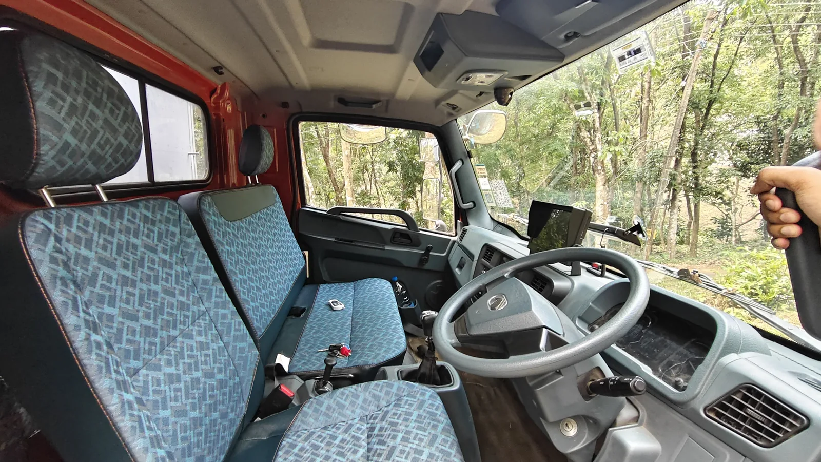 The driving cab with bench seating and forest visible through the windscreen.