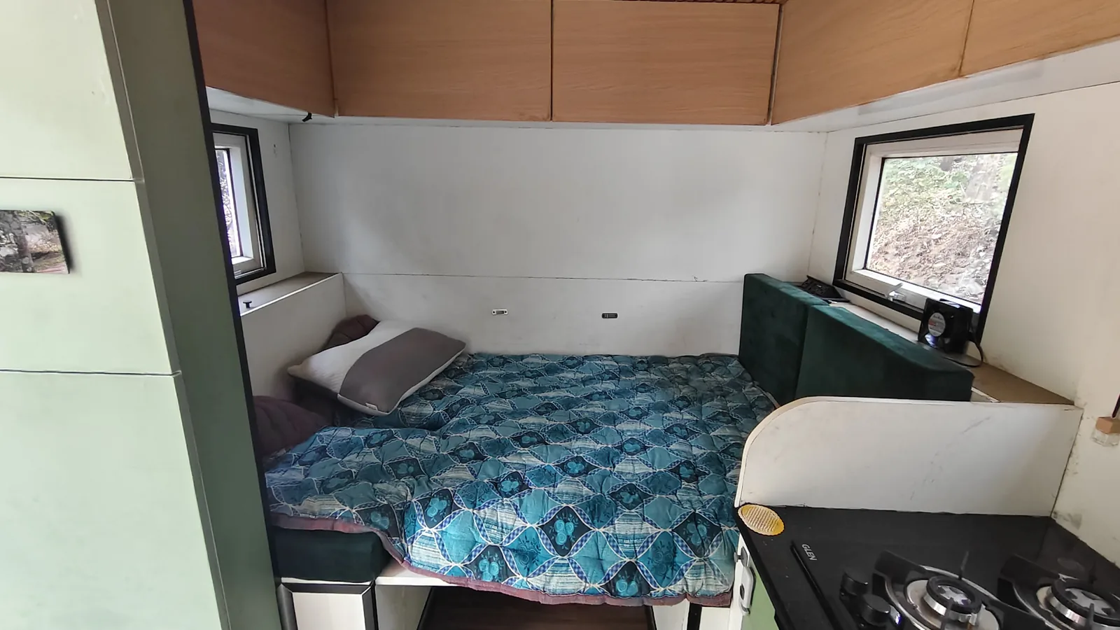 Inside Bhanumati: the full-width bed with sage green cabinetry, windows either side and the galley beyond.