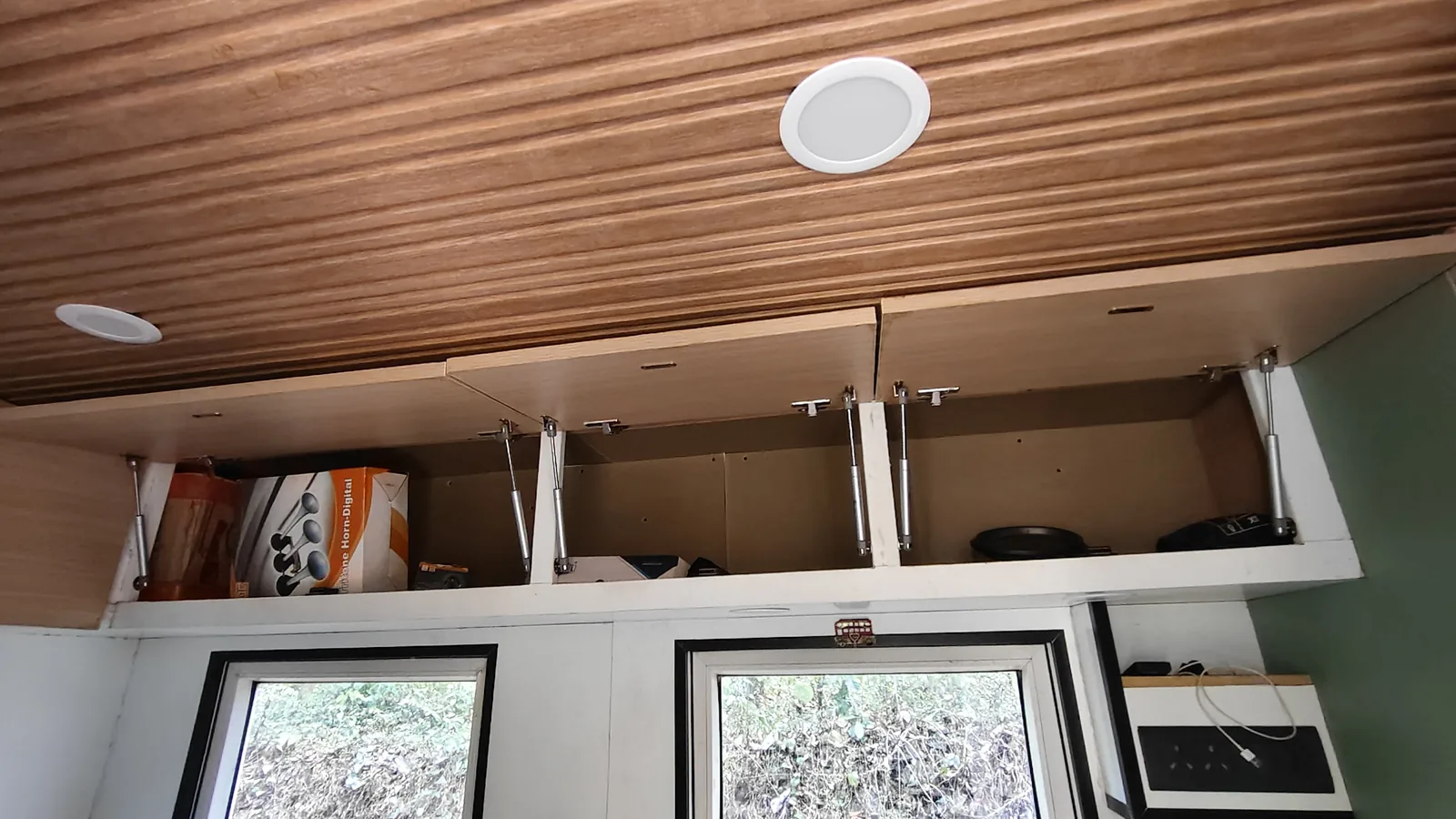 The timber-panelled ceiling with overhead cabinets, windows and interior lighting.