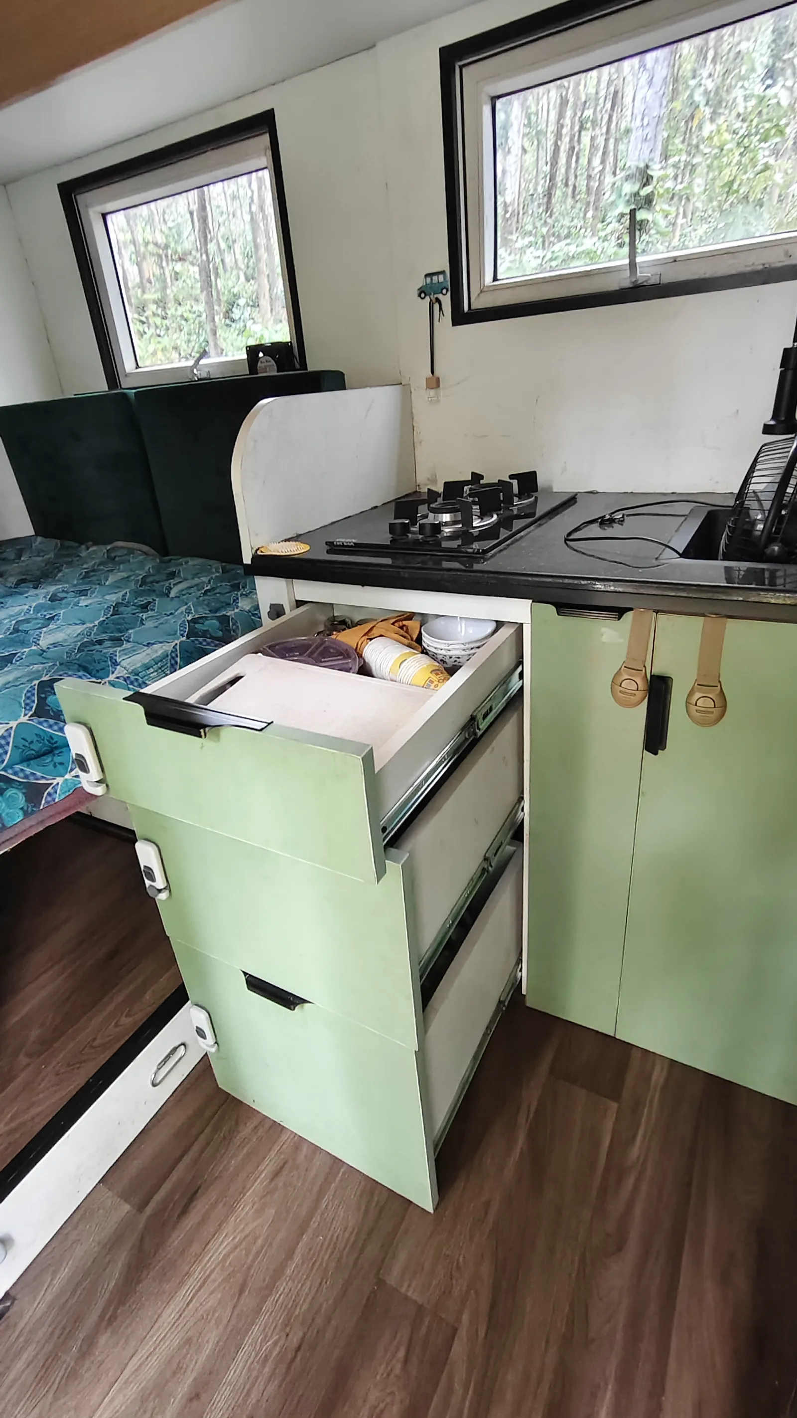 The kitchen run with gas hob, sink and cabinets over a timber floor.